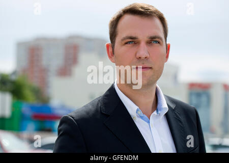 Close-up Portrait des jungen Geschäftsmann in einen dunklen Anzug und weißem Hemd auf dem Hintergrund der Sommer Stadt Stockfoto