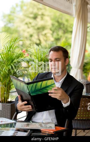 Junge Unternehmer hält ein Menü in einem Sommerrestaurant sitzen Stockfoto