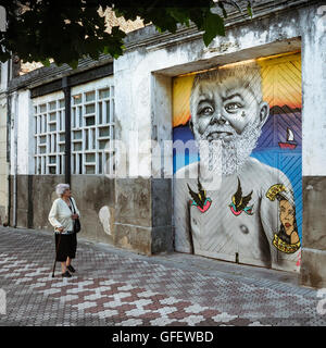 Gemälde eines Matrosen an der Eingangstür einer Lagerhalle und eine alte Dame schaut ihn an. Laredo, Kantabrien, Spanien. Stockfoto