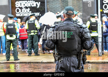 Belfast, Nordirland. 10. August 2014 - Polizeibeamte halten eine Menschenmenge unter Kontrolle, während ein Mitglied der taktischen Unterstützungsgruppe (Aufruhr) den Fortschritt beobachtet Stockfoto