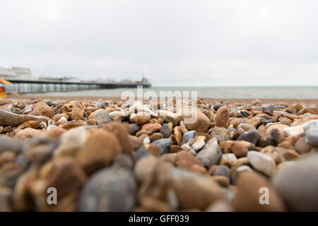 Wellen und Meer wäscht über Kies und Steinstrand an einem stürmischen Tag grau in Sussex, Brighton Pier im Fokus. Stockfoto