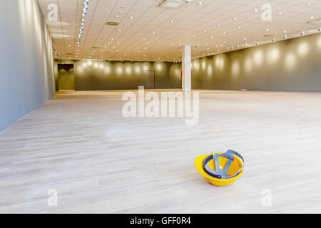 Gelb Schutzhelm befindet sich auf dem Kopf stehend auf dem Boden eines großen Showrooms in ein modernes Businesscenter mit Deckenleuchte. Stockfoto