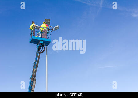 Hohe erhöhten Hubarbeitsbühne mit Team von Arbeitern auf Flutlicht. Stockfoto