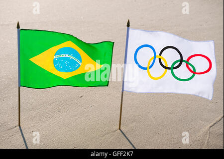 RIO DE JANEIRO - 24. März 2016: Olympische Flagge steht flattern mit der brasilianischen Flagge in den Wellen am Strand von Ipanema Strand. Stockfoto