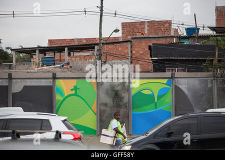 Bewohner von Complexo da Mare, einer massiven Netzwerk der Favelas, die neben der Linha Vermelha (rote Linie), die Autobahn vom Flughafen in die Innenstadt, Rio De Janeiro sitzt arbeiten als Straßenverkäufer während der Stoßzeiten an der Expreessway - seit 2010 ist die Gemeinschaft eingezäunten Weg von der Autobahn durch riesige Plexiglas Platten - Behörden behaupten sie bieten eine akustische Barriere , einheimischen beschreiben es als eine "Mauer der Schande", anders Arme Menschen zu verstecken. Kurz vor den Olympischen Spielen begann die Stadt Verputzen die 3 Meter hohen, 7km langen Tafeln mit bunten Olympia-Plakate s Stockfoto