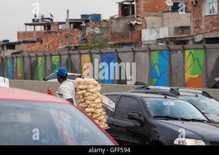 Bewohner von Complexo da Mare, einer massiven Netzwerk der Favelas, die neben der Linha Vermelha (rote Linie), die Autobahn vom Flughafen in die Innenstadt, Rio De Janeiro sitzt arbeiten als Straßenverkäufer während der Stoßzeiten an der Expreessway - seit 2010 ist die Gemeinschaft eingezäunten Weg von der Autobahn durch riesige Plexiglas Platten - Behörden behaupten sie bieten eine akustische Barriere , einheimischen beschreiben es als eine "Mauer der Schande", anders Arme Menschen zu verstecken. Stockfoto