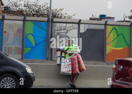 Bewohner von Complexo da Mare, einer massiven Netzwerk der Favelas, die neben der Linha Vermelha (rote Linie), die Autobahn vom Flughafen in die Innenstadt, Rio De Janeiro sitzt arbeiten als Straßenverkäufer während der Stoßzeiten an der Expreessway - seit 2010 ist die Gemeinschaft eingezäunten Weg von der Autobahn durch riesige Plexiglas Platten - Behörden behaupten sie bieten eine akustische Barriere , einheimischen beschreiben es als eine "Mauer der Schande", anders Arme Menschen zu verstecken. Stockfoto