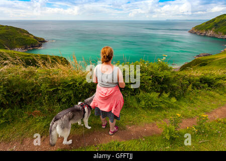 Ein Frau Hund zu Fuß entlang der Küste um Lantic Bay, Cornwall, UK mit der Kamera in Schuss an einem Sommertag Stockfoto