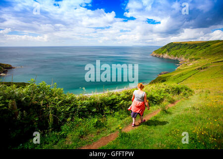 Eine Frau, die zu Fuß entlang der Küste um Lantic Bay, Cornwall, UK mit der Kamera an einem Sommertag Schuß Stockfoto