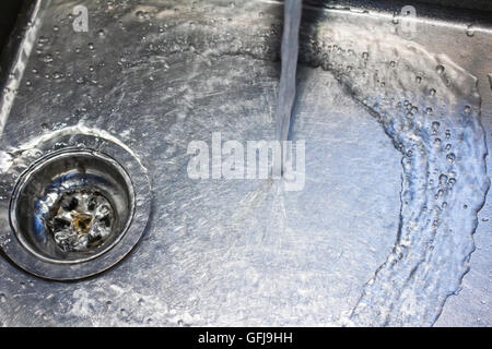 Wasser aus einem Hahn läuft den Bach runter in eine Edelstahl-Spüle Stockfoto