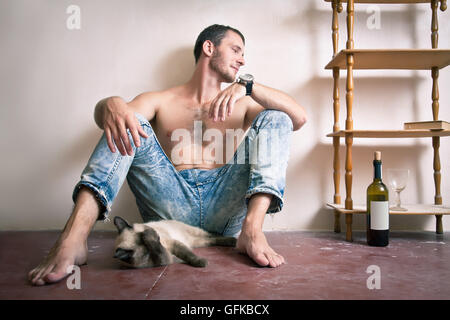 Porträt eines jungen Mannes sitzen auf dem Boden mit einer Katze und einer Flasche Wein Stockfoto