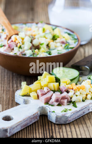 Traditionelle russische Sommer kalte Suppe Okroschka mit Kefir in Keramikschale auf rustikalen Holztisch, Zutaten Stockfoto