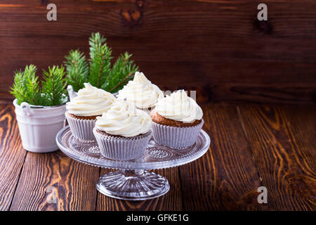 Hausgemachte Weihnachts Cupcakes mit Frischkäse frosting auf hölzernen Hintergrund mit Fichte Zweige in Keramik Eimer und Apfel-Cidre Stockfoto