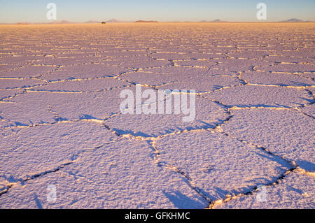 Salar de Uyuni: den Sonnenaufgang bei der Salt See schafft ein schönes Muster. In der Ferne treibt ein Jeep über den Salzsee Stockfoto