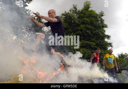 Ein Konkurrent springt über Feuer während der harte Kerl Brennnessel Krieger 2016 um South Perton Farm in Staffordshire. Stockfoto