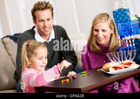 Eine junge Familie feiert Chanukka zu Hause, mit Geschenken, Lesung, Dreidel, etc.. Stockfoto