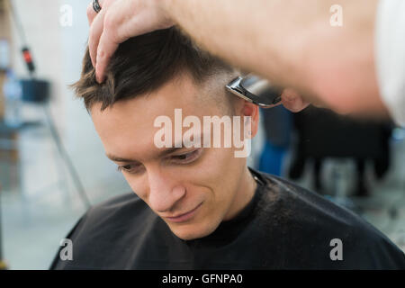 Professionelles Styling. Seitenansicht des jungen Mannes immer Haarschnitt von Friseur mit Elektrorasierer bei Barbershop hautnah Stockfoto