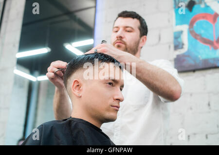 Professionelles Styling. Seitenansicht des jungen Mannes immer Haarschnitt von Friseur mit Elektrorasierer bei Barbershop hautnah Stockfoto