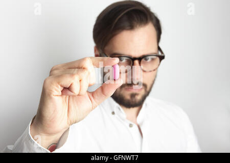 Junge bärtigen Mann mit weißem Hemd Brille mit rosa Farbe Pill.Medicine Gesundheit Pflege Menschen Konzept Photo.Adult ernst Arzt leer Background.Horizontal. Stockfoto