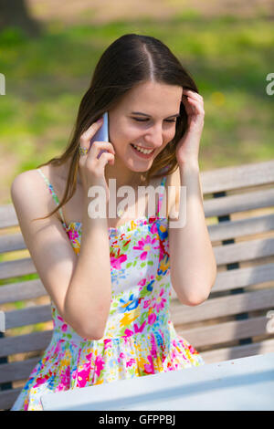 Eine Mädchen trägt Farbe Kleid verwendet Handy im Sommerpark Stockfoto