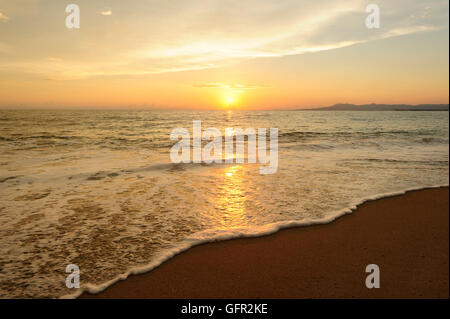 Meer Sonnenuntergang ist ein hell am Strand mit den Sonnenuntergang am Meer Horizont wie eine sanfte Welle entlang der sandigen Küste rollt. Stockfoto