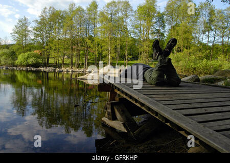 Junger Mann chillen auf einem Steg am See in Schweden Stockfoto