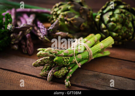 Spargel und Artischocken mit Kräutern auf einem hölzernen Hintergrund Stockfoto