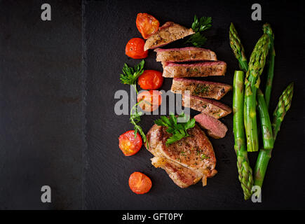 Saftiges Steak Medium selten Rindfleisch mit Gewürzen und Tomaten, Spargel. Ansicht von oben Stockfoto
