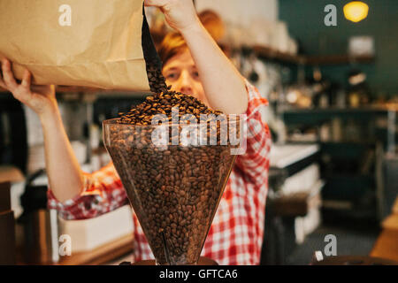 Eine Frau, die Kaffeebohnen in einem Mahlwerk Trichter in einem Café gießen Stockfoto
