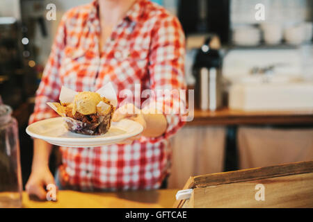 Eine Frau in einem Coffee-Shop hält eine Platte mit einem frischen Muffin mit einer Kugel Eis Stockfoto