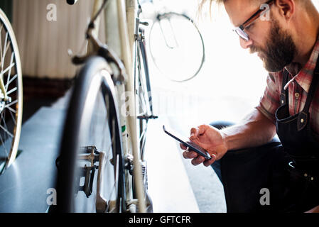 Einem Fahrradmechaniker in eine Fahrradwerkstatt mit einem Smartphone Stockfoto