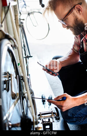 Einem Fahrradmechaniker in eine Fahrradwerkstatt mit einem Smartphone Stockfoto