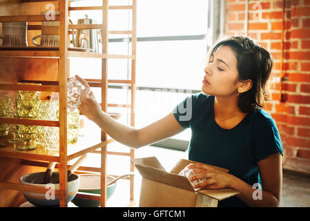 Junge Frau in einem Geschäft ein Trinkglas auf einem Regal platzieren Stockfoto