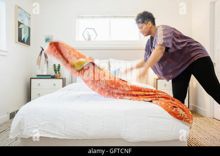 Eine Frau, die einen floralen gemusterten Quilt auf ein Doppelbett in einem hellen luftigen Schlafzimmer verteilen Stockfoto