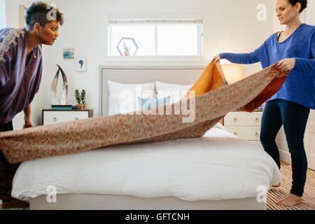 Zwei Frauen, aus denen ein Bett verbreiten eine gemusterte Decke über dem Doppelbett in einem hellen luftigen Schlafzimmer mit weißen Wänden Stockfoto