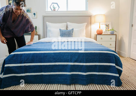 Eine Frau, die Glättung einer blaues gestreift werfen über ein Doppelbett im Schlafzimmer Stockfoto