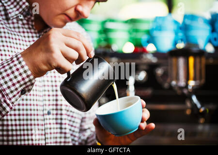 Ein Mann Gießen heißen Milch in eine Tasse Kaffee zu einem Muster auf der Oberseite Stockfoto