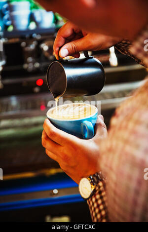 Ein Barista in Gießen heißen Milch, den Schaum auf eine Tasse Kaffee, eine Muster zu machen Stockfoto