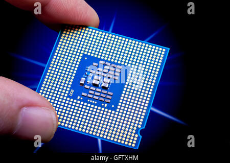 Leuchtende blaue Computer CPU statt zwischen Finger und Daumen vor Starburst auf einem schwarzen Hintergrund Stockfoto