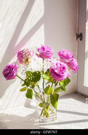 Bild der romantischen Szene mit rosa Rosen in einer Vase von einem alten Fenster. Stockfoto