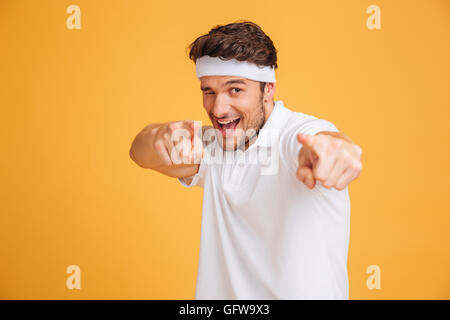 Porträt der verspielte junge Athlet zwinkert und zeigen Sie auf gelbem Hintergrund Stockfoto