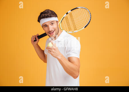 Attraktive junge glücklich Tennisspieler Schläger halten und zeigen Sie auf gelbem Hintergrund Stockfoto