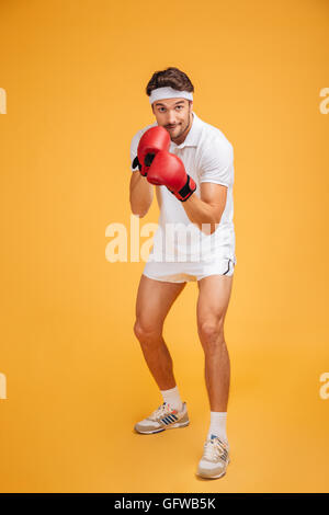 Junger Mann Boxer konzentriert in rote Handschuhe bereit für den Kampf auf gelbem Hintergrund Stockfoto