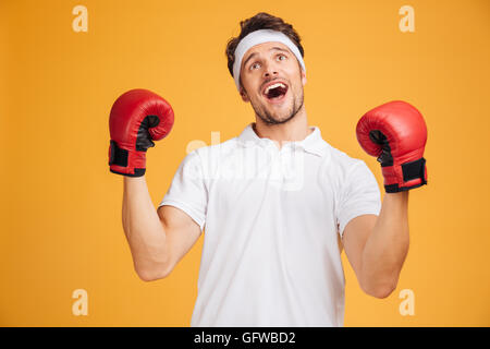 Fröhlich begeistert junge Mann Boxer in rote Handschuhe schreien und feiern Erfolg über gelbem Hintergrund Stockfoto