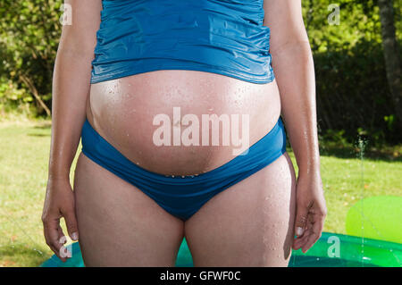 Eine 8,5 Monate schwangere Frau im Sommer kühl zu halten. Eine Nahaufnahme von den schwangeren Bauch in einem Badeanzug. Stockfoto