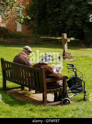 Ein älteres Paar (Mann, Frau) Entspannung auf einer Bank auf dem Friedhof der southwell Minster. Stockfoto