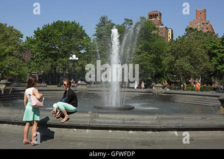 Zwei unbekannte junge Frauen neben dem Brunnen im Washington Square Park, New York, im Gespräch Stockfoto