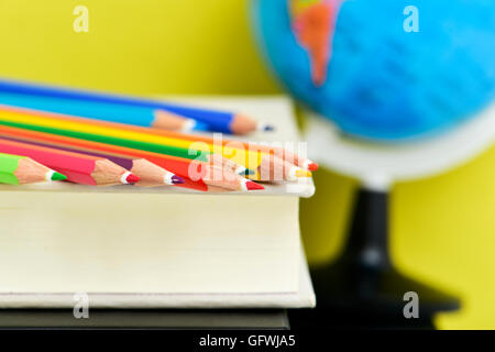 Nahaufnahme von einem Haufen von Bleistift Buntstifte in verschiedenen Farben auf einem Stapel von Büchern und eine Erdkugel im Hintergrund gegen eine Stockfoto