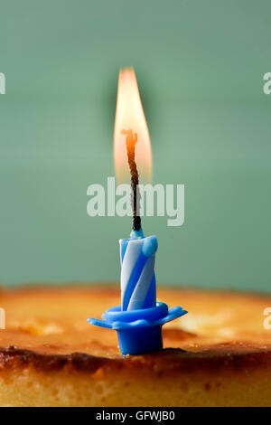 Nahaufnahme von einem Käsekuchen garniert mit einer beleuchteten Geburtstag Kerze vor einem rustikalen blass grün Holz Hintergrund Stockfoto