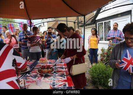 Straßenfest statt zur Feier von Königin Elizabeth II 90. Geburtstag - Frau trägt eine Maske und gekleidet wie der Königin schneiden Kuchen Leute zuschauen Cornwall Straße Surrey England Stockfoto